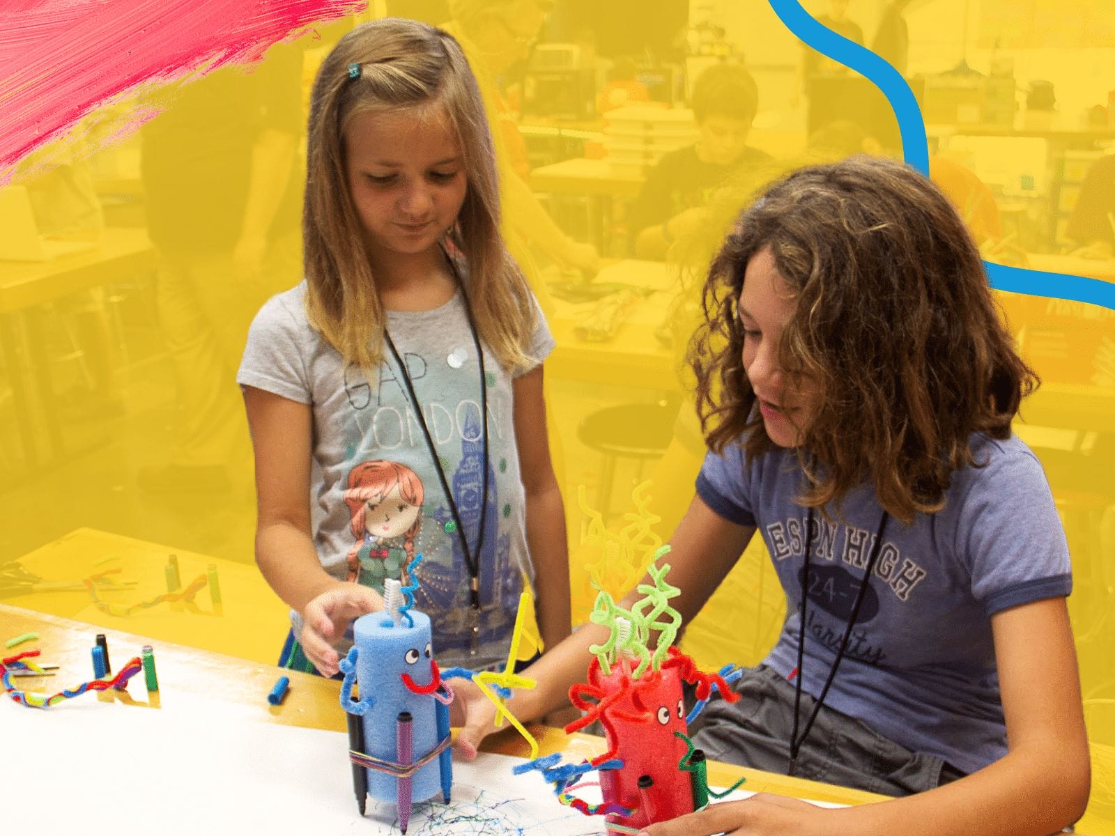 Two girls are working on a colorful arts and crafts project at a table in a classroom, blending creativity with lessons from their entrepreneurship education. One is standing, while the other is sitting. In the background, other children are engaged in various activities.