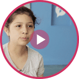 A person with dark hair tied back is speaking while wearing a light gray shirt. Blue background with an inset speech bubble icon. A play button icon appears over the image, promoting youth entrepreneurship education.