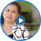 A person with long dark hair wears a white and black patterned shirt, speaking and looking slightly to the side, possibly discussing the importance of entrepreneurship education.
