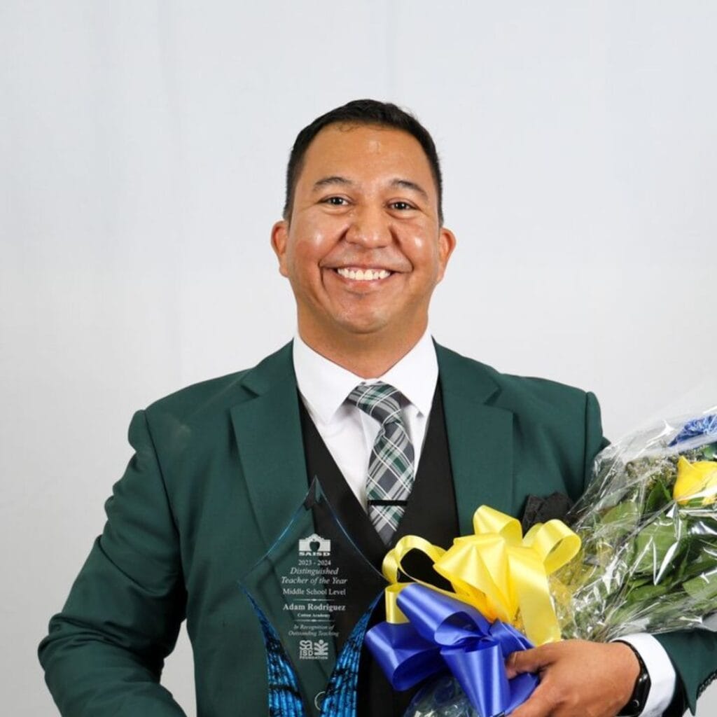 A person in a suit holds an award and a bouquet of flowers, smiling at the camera, after speaking at San Antonio's Middle School Career Exploration Program.