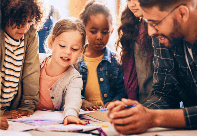 Children and a teacher engaged in a group activity around a table, with papers and markers visible, reflect the spirit of VentureLab collaboration, fostering creativity and learning through dynamic education partnerships.