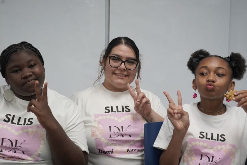 Three girls waving a peace sign at a pitch competition in St. Louis